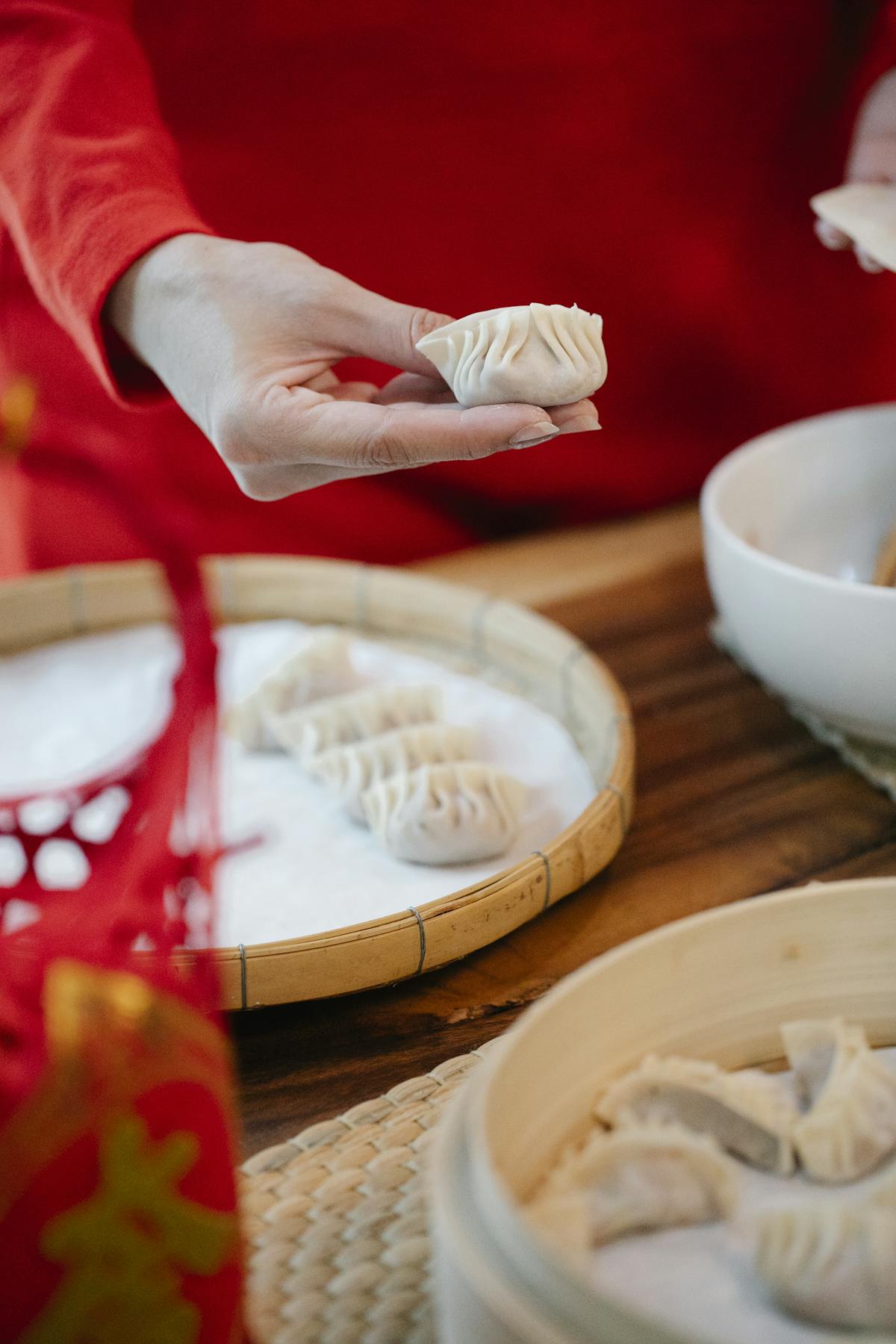 High angle of crop anonymous female putting raw homemade jiaozi dumplings in bamboo steamer while cooking Asian food in kitchen